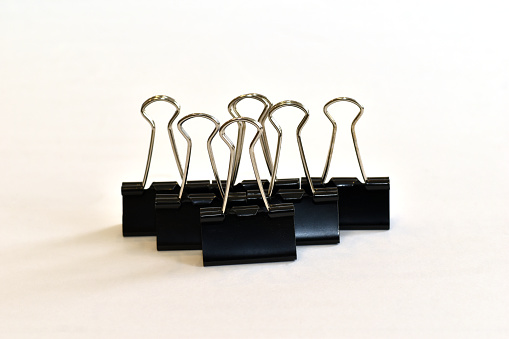 Large stationery clips, paper clips, black, lined up in several rows on a white background.