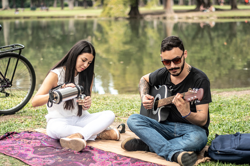 Young man singing while playing acoustic guitar to his girlfriend on the public park