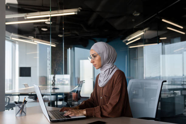 Serious and thinking woman in hijab working inside office with laptop, Muslim female programmer typing on keyboard writing software code at workplace working artificial intelligence development. mujer seria y pensante con hijab que trabaja dentro de la oficina con una computadora portátil, programadora musulmana escribiendo en el teclado escribiendo código de software en el lugar de trabajo trabajando en el desarrollo de inteligencia artificial
