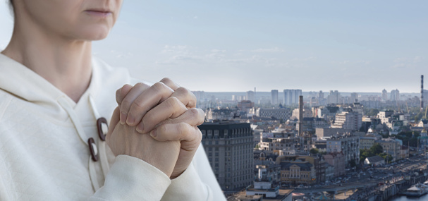 A woman prays against the backdrop of the city.