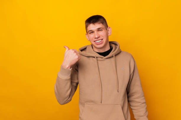 istock Wide smiling man is pointing backwards with his thumb over yellow copy space. 1483125080