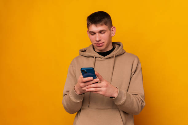 Young handsome concentrated man is using his smart phone in a yellow studio. stock photo