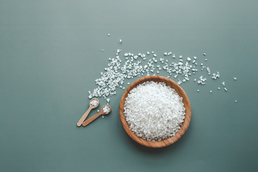White sea salt in wooden plate on green background, home spa.