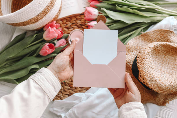 woman's hands holding a letter in craft envelope. pink background, mother's day concept. place for your text - bouquet mothers day tulip flower imagens e fotografias de stock