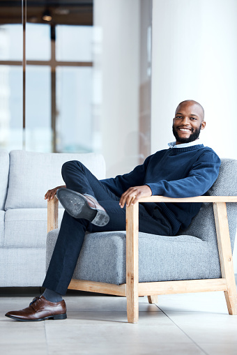 Portrait, black man in office and waiting on chair, smile and confident for job interview, resting and relax. Face, African American male employee and entrepreneur in workplace, happiness and joyful
