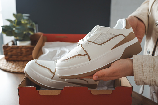 Unpacking women's shoes, stylish white sneakers in hands.