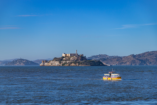 A picture of the Alcatraz Island and the surrounding San Francisco Bay, with a water taxi sailing near the foreground.