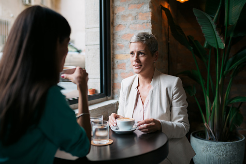 Mature businesswoman meeting with a female colleague at a coffee shop. Two businesswomen discussing over a cup of coffee at city cafe.