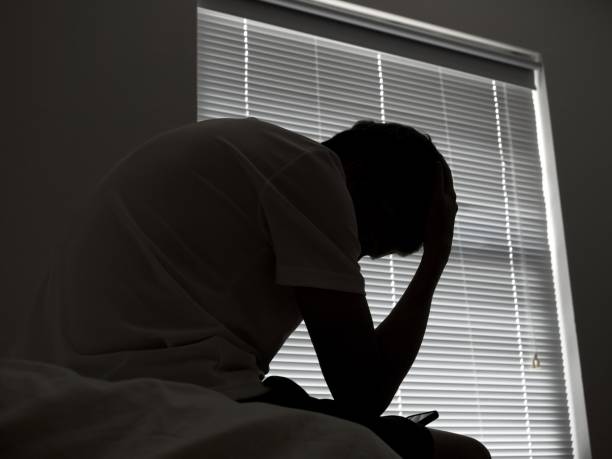 istock A distressed man in silhouette sits in dark room texting on smartphone 1483132571