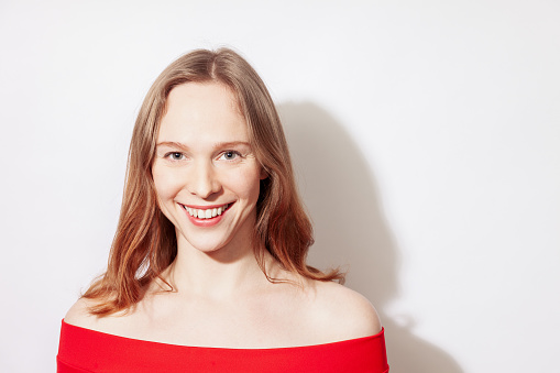 Close-up studio portrait of a happy young white woman with long brown hair in a red dress against a white background