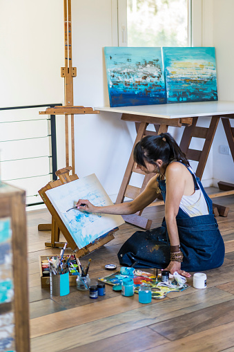 Woman artist painting on a canvas a blue abstract painting. Creative ywoman working on the floor in her art studio.