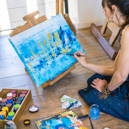 Woman artist painting on a canvas a blue abstract painting. Creative woman working on the floor in her art studio.