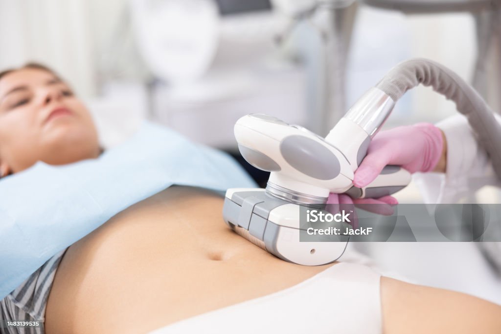 Unrecognizable masseur performing anti cellulite massage for belly of young woman in aesthetic medicine clinic Young woman getting ultrasound cavitation body contouring treatment, anti-cellulite therapy, vacuum massage from unrecognizable cosmetologist. Hardware cosmetology for body sculpting The Human Body Stock Photo