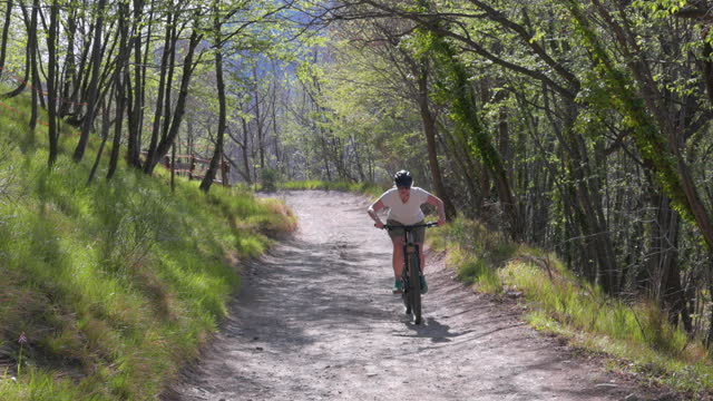Senior woman e-mountain bikes along forest track