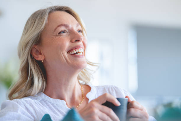 donna matura che si gode una tazza di tè o caffè seduta sul divano. - mature women beautiful senior women menopause foto e immagini stock