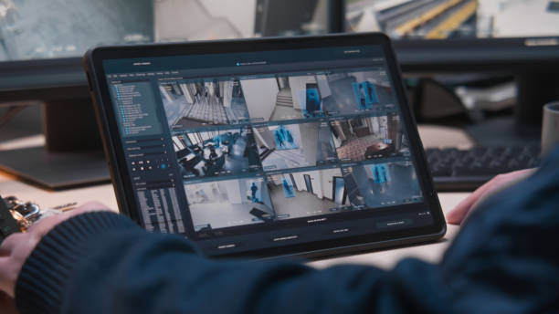 Digital tablet with CCTV cameras playback Male security officer controls CCTV cameras in office, uses digital tablet and computers with surveillance camera footage playback on screens. High tech security system. Monitoring and social safety. indoor security camera stock pictures, royalty-free photos & images