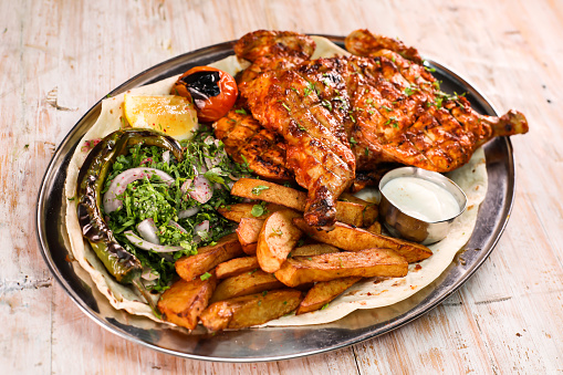 Full grilled chicken with salad, wedges, lemon and dip served in dish isolated on background top view of arabic food