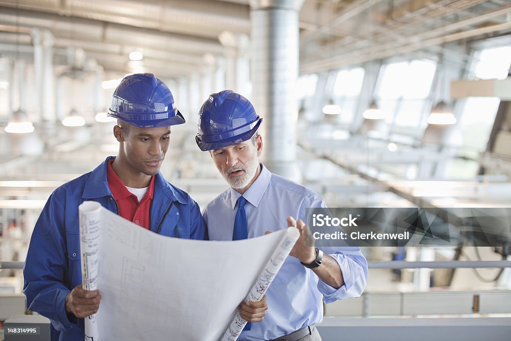 Architecte ou Ingénieur examinant un plan d'architecte en usine - Photo de Plan d'architecte libre de droits