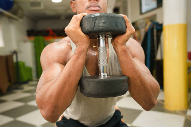 Active dumbbell squats: A strong handsome African man squatting with a dumbbell at the chest level.