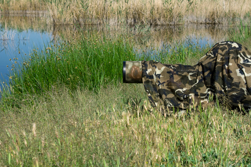 Camouflaged wild life photographer waiting for birds by lake