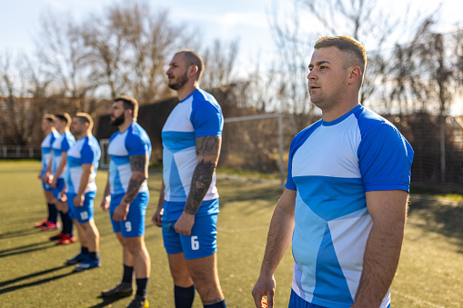 Group of men, male rugby team standing in a row on sports field outdoors.