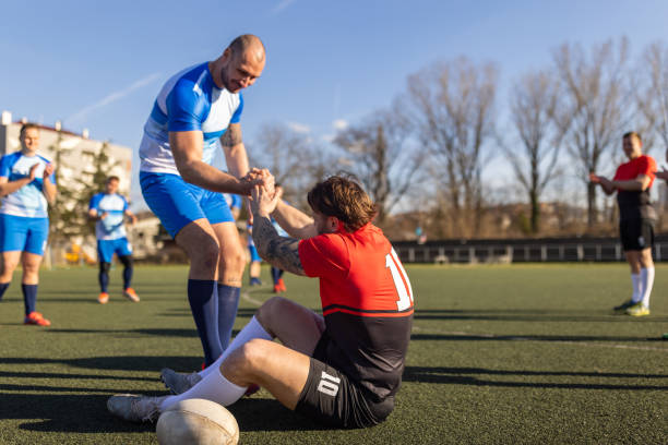 Group of men, male rugby player helping injured player from rival team during the match.