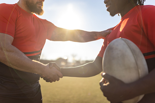 Two men, male rugby team shaking hands after the match on sports field outdoors.