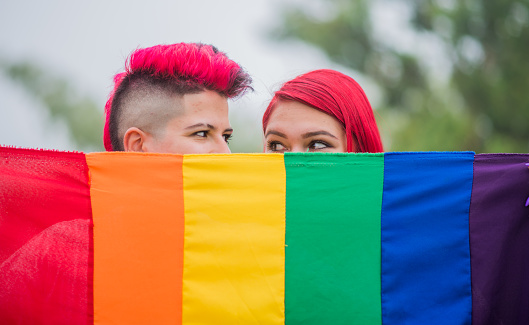 close up portrait of woman couple with gay pride flag outdoors, two young women with gay pride flag.