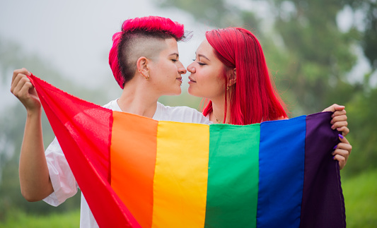 close up portrait of woman couple with gay pride flag outdoors, two young women with gay pride flag.