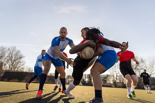 Group of men, male rugby teams playing a match on the sports field outdoors.