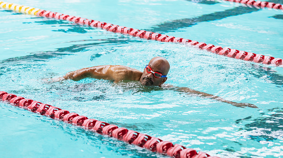 A senior African-American man, in his 60s, swimming laps. He is in a lane, between two lane markers, swimming freestyle.