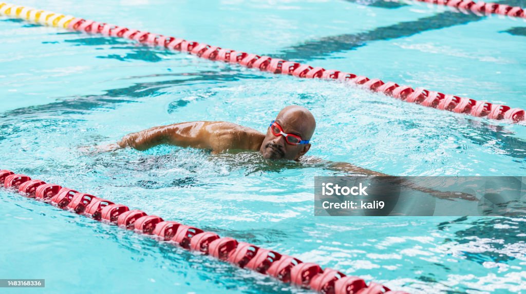 Senior African-American man at pool swimming laps A senior African-American man, in his 60s, swimming laps. He is in a lane, between two lane markers, swimming freestyle. Swimming Stock Photo