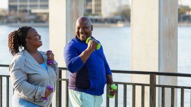 African-American couple power walking on waterfront A mature African-American couple exercising together outdoors, power walking with hand weights on a city waterfront. They are smiling, enjoying their workout. body positive couple stock pictures, royalty-free photos & images