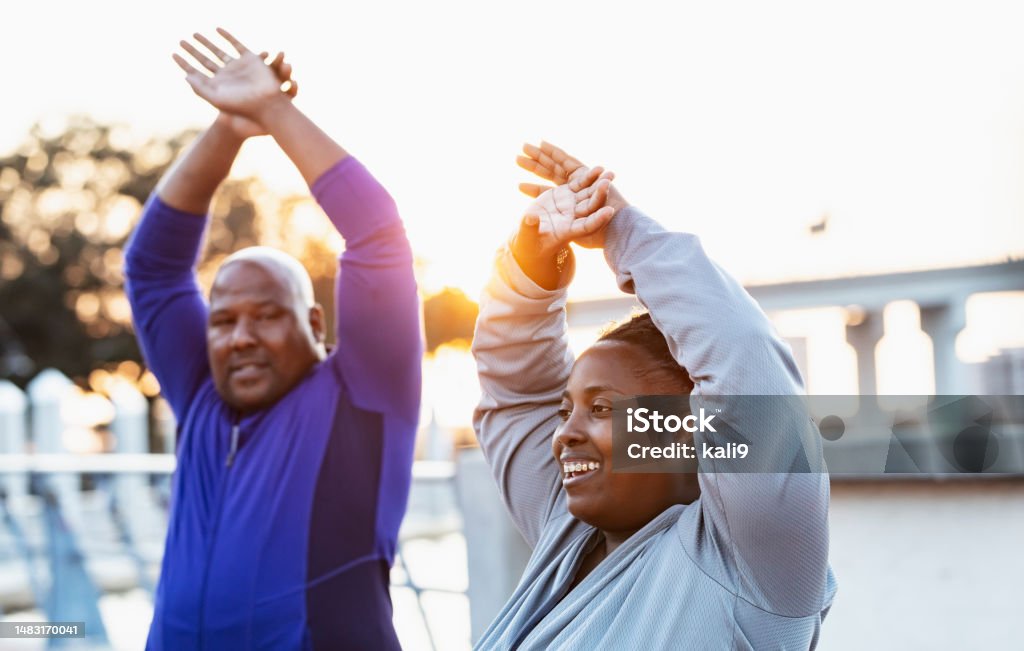 Mature African-American couple stretching, focus on woman A mature African-American couple exercising outdoors, stretching their arms above their heads. The focus is on the woman. Stretching Stock Photo