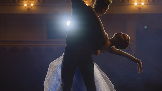 Beautiful ballet dancers practice and rehearse choreography on classic theater stage illuminated by spotlights. Man and woman prepare for theatrical dance performance. Art of classical ballet dance.