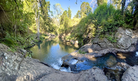 Horizontal photo of a freshwater creek and natural rock pool with regrowth of grass, rainforest trees and plants, one year after devastating floods removed and destroyed the landscape. Huonbrook Valley, Byron Bay hinterland, northern NSW.