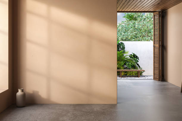 istock Spacious empty room with beige walls, concrete flooring, and shadows of window frames casting on the walls. The view of the backyard adds a sense of calmness and tranquility to the space. 3d rendering 1483177197