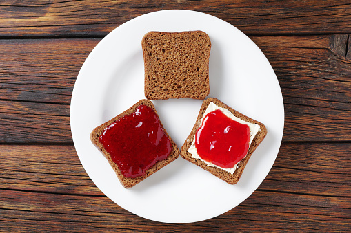 Slice of small rye bread with jam on a plate on a wooden background, top view