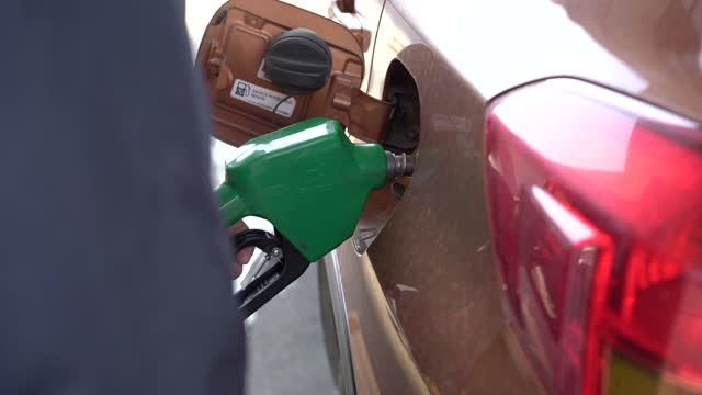 A man holds  fuel nozzle into the gas tank of a car at the gas station