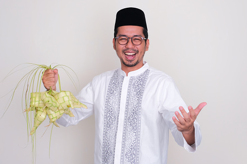 Moslem Asian man showing joyful expression while holding rhombus shaped rice cake