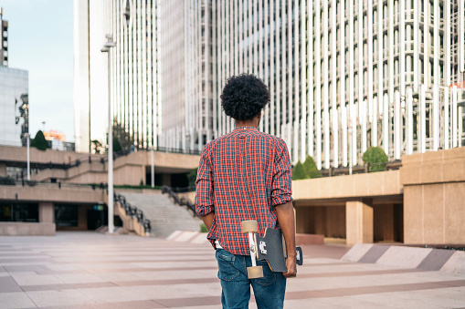 Stock photo of unrecognized skater boy walking in the city with his longboard.