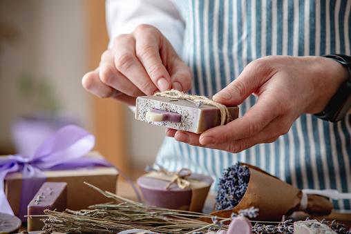 Woman in an apron is packing lavender natural soap and bouquets of lavender flowers. Concept of handmade presents.