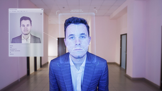Businessman scans his face in office. Security system software identifies person, shows personal profile. 3D hologram of human biometric facial recognition. Identification, privacy, and AI technology.