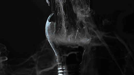Lamp explosion smoke cloud. Power failure. Defocused gray color vapor haze in broken glass light bulb on dark black night abstract background.
