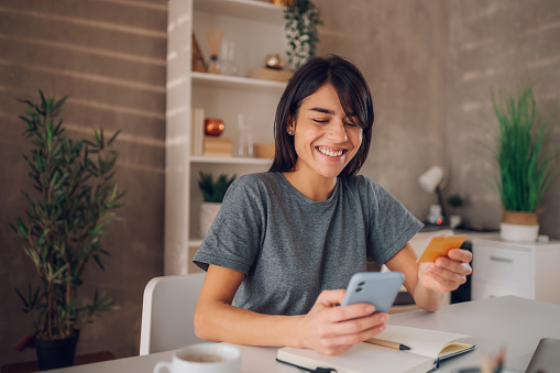 Close up shot of a beautiful businesswoman with a big smile on her face looking at her cell phone and placing an online order while holding a credit card in the other hand. Copy space.