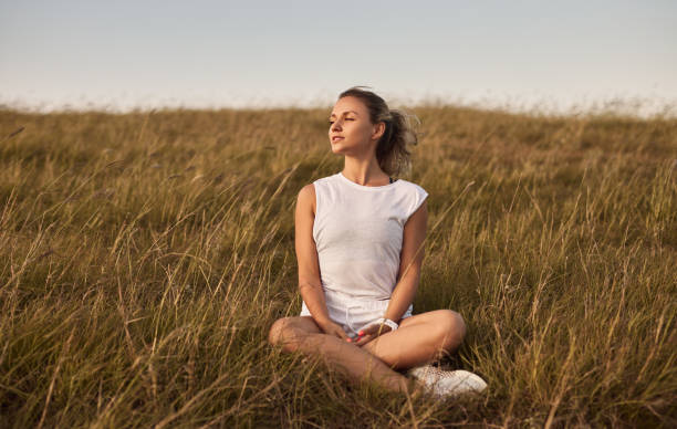 woman resting on grassy field - zen like nature breathing exercise sitting imagens e fotografias de stock