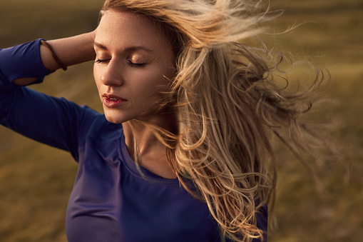 Relaxed young female with long blond hair fluttering in wind enjoying summer day in nature