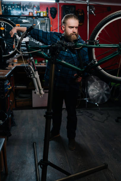 portrait vertical d’un réparateur regardant le levier de vitesses arrière d’un vélo de montagne, changeant de vitesse à l’aide d’un levier de vitesses de guidon travaillant dans un atelier de réparation de vélos - cycling bicycle occupation men photos et images de collection