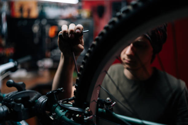 plan recadré en gros plan d’un réparateur professionnel méconnaissable réparant un vélo à l’aide d’un outil spécial travaillant dans un atelier de réparation de vélos avec un intérieur sombre. - cycling bicycle occupation men photos et images de collection