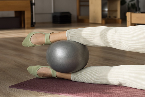Pilates drill with mini-ball. Woman in sportswear using a small fit ball in pilaes yoga studio. Trainer holding fitness ball between legs.
